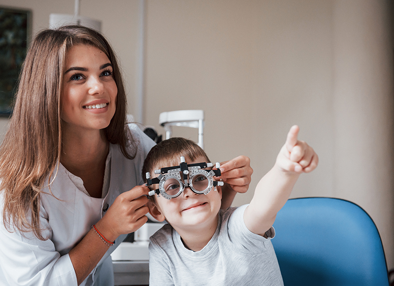 Eine Optikerin berät ein Kind mit einem Phoropter